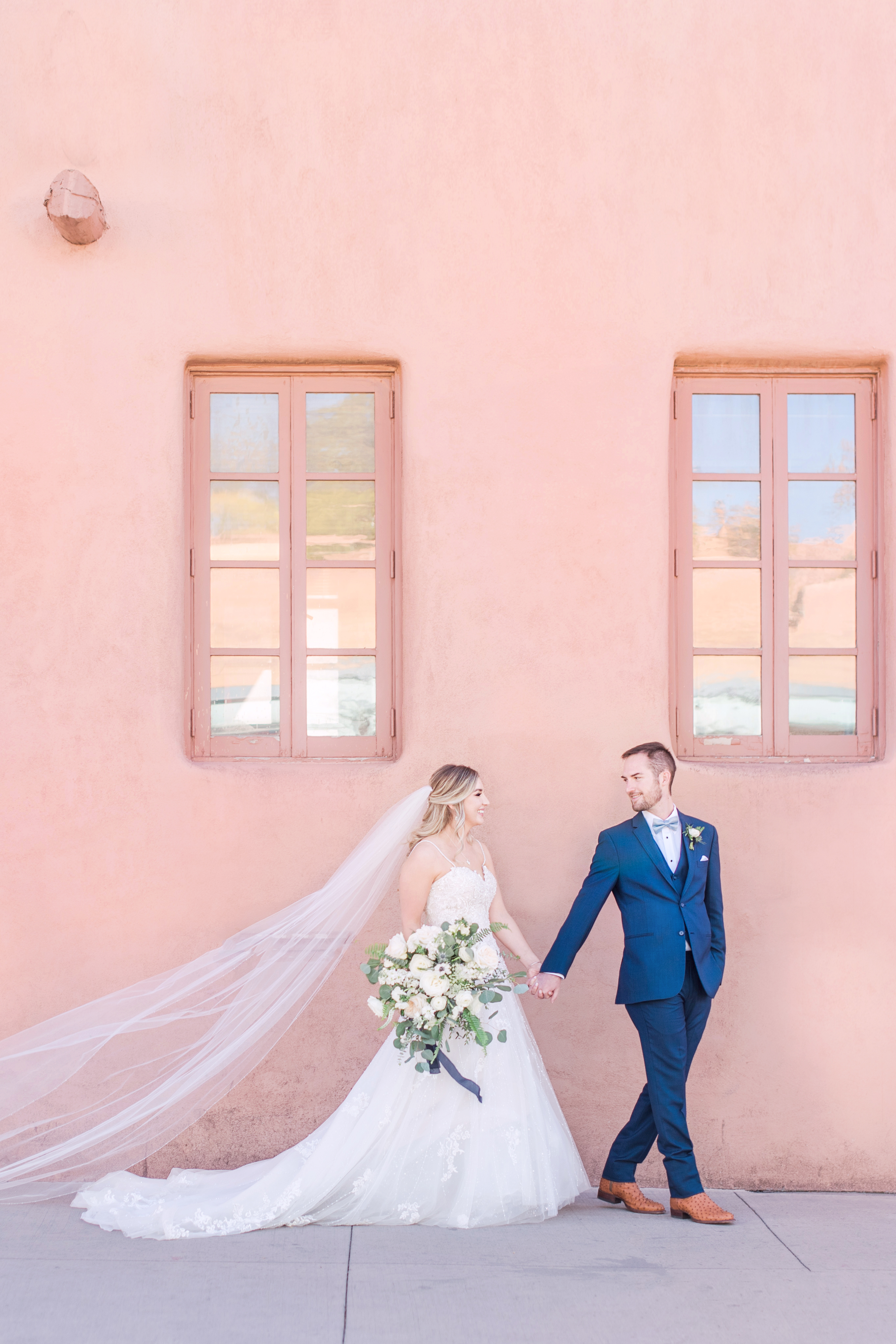 Couple walking in downtown santa fe with pink adobe building