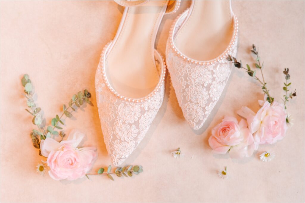 lace detailed wedding shoes on a pink mat surrounded by flowers