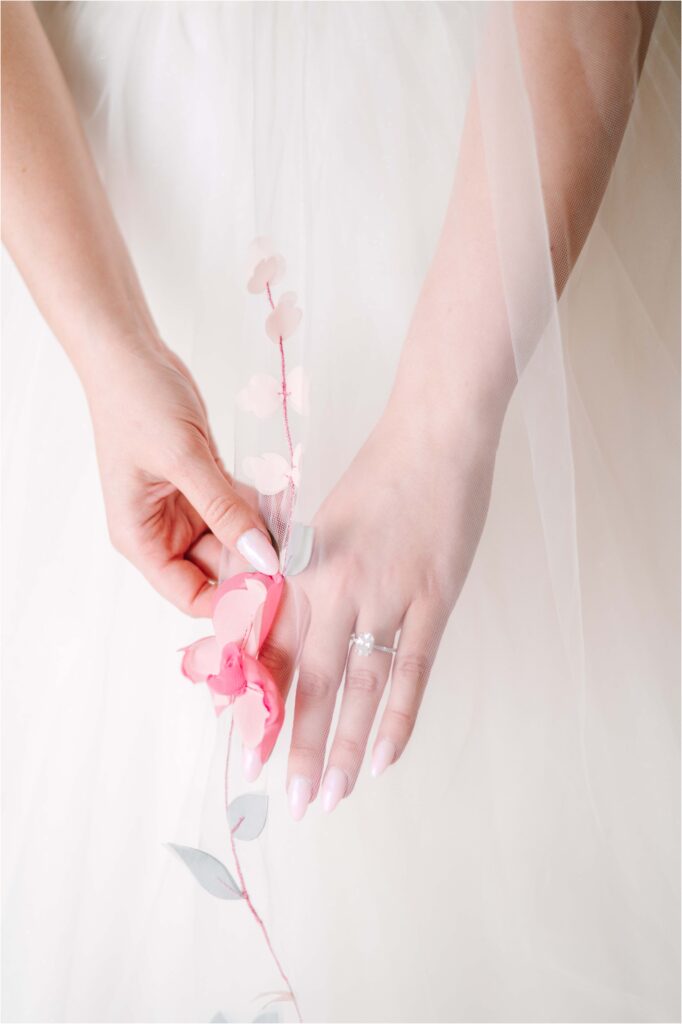 bride's hands behind her veil holding an embroidered flower
